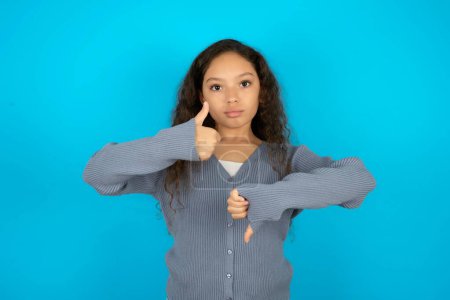 Photo for Teenager girl wearing grey sweater against blue background showing thumbs up and thumbs down, difficult choose concept - Royalty Free Image