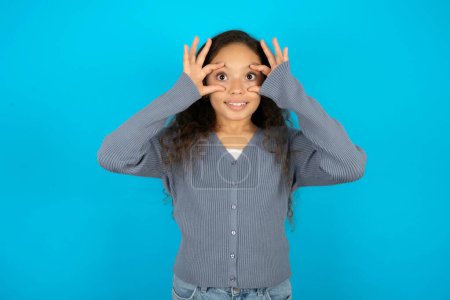 Téléchargez les photos : Adolescente portant un pull gris sur fond bleu gardant les yeux ouverts pour trouver une opportunité de succès. - en image libre de droit
