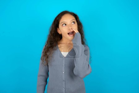 Téléchargez les photos : Adolescent fille portant pull gris sur fond bleu entendre incroyable nouvelles privées impressionné partager cri - en image libre de droit