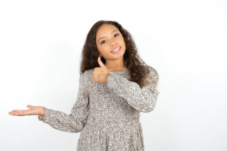 Photo for Teenager girl wearing grey dress against white background Showing palm hand and doing ok gesture with thumbs up, smiling happy and cheerful. - Royalty Free Image