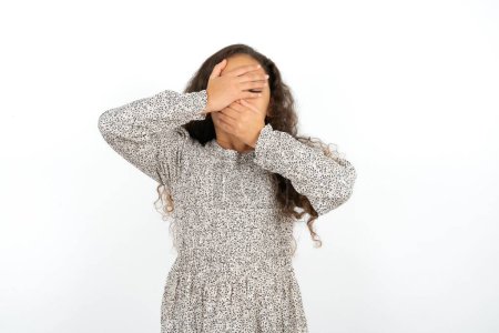 Photo for Teenager girl wearing grey dress against white background Covering eyes and mouth with hands, surprised and shocked. Hiding emotions. - Royalty Free Image