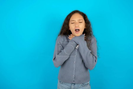Foto de Adolescente usando suéter gris contra fondo azul gritando sofocar porque estrangulamiento doloroso. Problema de salud. Concepto de asfixia y suicidio. - Imagen libre de derechos