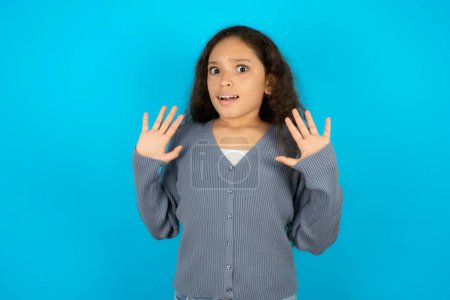 Photo for Teenager girl wearing grey sweater against blue background afraid and terrified with fear expression stop gesture with hands, shouting in shock. Panic concept. - Royalty Free Image