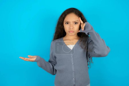 Photo for Teenager girl wearing grey sweater against blue background confused and annoyed with open palm showing copy space and pointing finger to forehead. Think about it. - Royalty Free Image