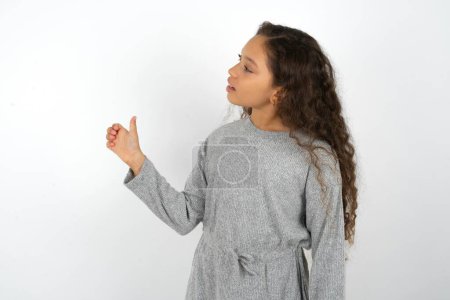 Foto de Adolescente chica usando gris suéter buscando orgulloso, sonriendo haciendo pulgares hacia arriba gesto a un lado. Buen trabajo.! - Imagen libre de derechos