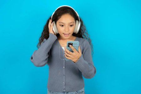 Foto de Chica adolescente feliz usando suéter gris se siente bien mientras se centra en la pantalla del teléfono inteligente. Personas, tecnología, estilo de vida - Imagen libre de derechos