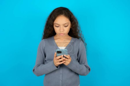 Photo for Focused teenager girl wearing grey sweater use smartphone reading social media news, or important e-mail - Royalty Free Image