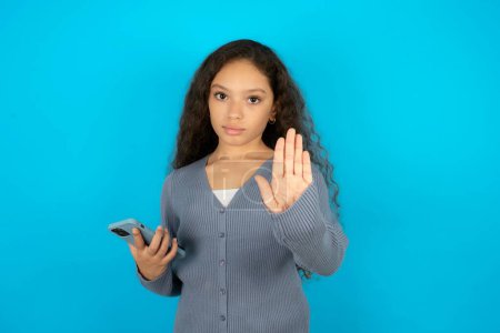 Photo for Teenager girl wearing grey sweater using and texting with smartphone with open hand doing stop sign with serious and confident expression, defense gesture - Royalty Free Image