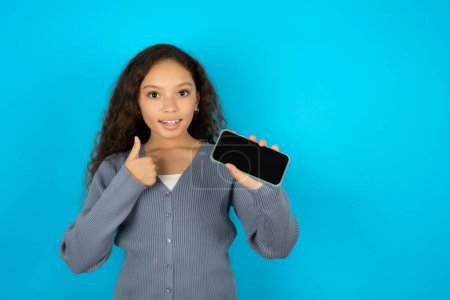 Photo for Portrait teenager girl wearing grey sweater holding in hands cell showing giving black screen thumb up - Royalty Free Image