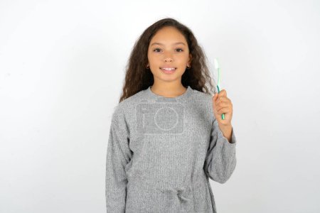 Foto de Adolescente con suéter gris sosteniendo un cepillo de dientes y sonriendo. Concepto de salud dental. - Imagen libre de derechos