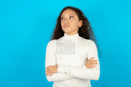 Photo for Charming thoughtful teenager girl wearing white sweater stands with arms folded concentrated somewhere with pensive expression thinks what to do - Royalty Free Image