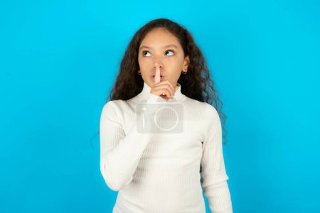 Téléchargez les photos : Adolescent fille portant pull blanc silence geste garde index aux lèvres fait signe de silence. Demande de ne pas partager le secret - en image libre de droit