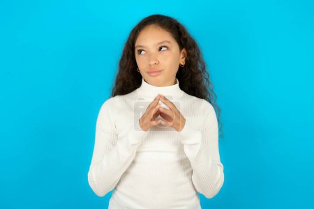 Photo for Teenager girl wearing white sweater steepled fingers and looks mysterious aside has great evil plan in mind - Royalty Free Image
