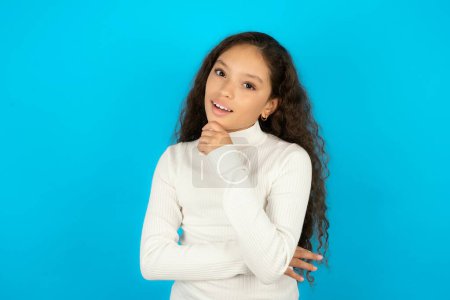 Photo for Teenager girl wearing white sweater laughs happily keeps hand on chin expresses positive emotions smiles broadly has carefree expression - Royalty Free Image
