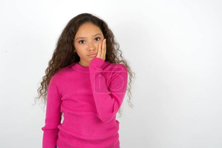 Photo for Sad lonely teenager girl wearing pink sweater touches cheek with hand bites lower lip and gazes with displeasure. Bad emotions - Royalty Free Image