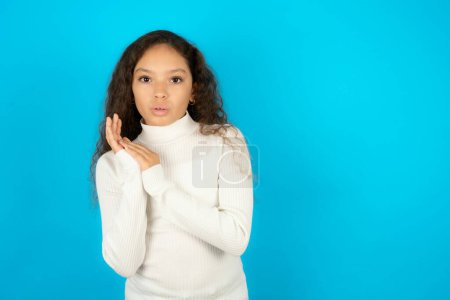 Téléchargez les photos : Surpris adolescent émotionnel fille portant pull blanc frotte les paumes et regarde la caméra avec incrédulité - en image libre de droit