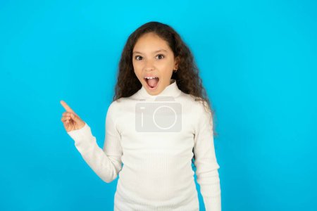 Photo for Teenager girl wearing white sweater points aside on copy blank space. People promotion and advertising concept - Royalty Free Image