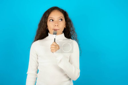 Téléchargez les photos : Photo d'adolescente rêveuse portant un pull blanc lécher la fourchette regarder espace vide - en image libre de droit