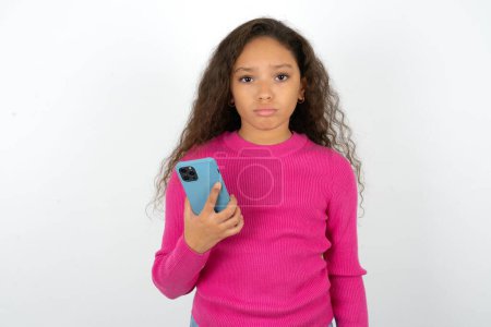 Foto de Niña adolescente molesta insatisfecha que usa suéter rosa utiliza la aplicación de software móvil y navega información en Internet, sostiene la mano móvil moderna - Imagen libre de derechos