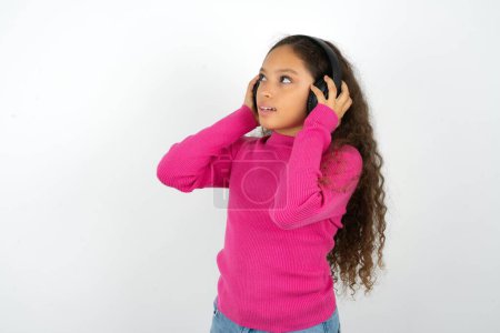 Foto de Adolescente con suéter rosa lleva auriculares estéreo escucha música concentrada a un lado. Gente hobby concepto de estilo de vida - Imagen libre de derechos