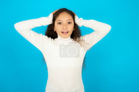 Photo for Cheerful overjoyed teenager girl wearing white sweater reacts rising hands over head after receiving great news. - Royalty Free Image