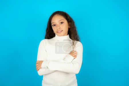 Foto de Retrato de una encantadora adolescente con suéter blanco de pie sonriendo con confianza con las manos dobladas - Imagen libre de derechos
