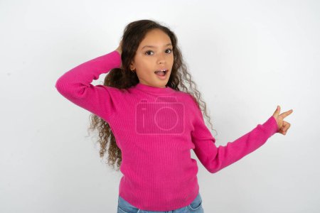 Foto de Sorprendido adolescente con suéter rosa apuntando al espacio vacío sosteniendo la mano en la cabeza - Imagen libre de derechos