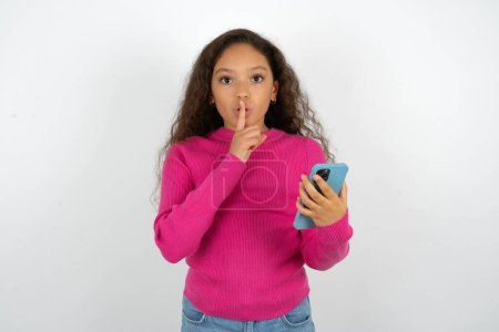 Téléchargez les photos : Adolescent fille portant pull rose tenant gadget moderne demander de ne pas dire de secrets - en image libre de droit