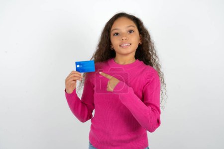 Téléchargez les photos : Portrait photo d'une adolescente portant un pull rose faisant des achats avec un doigt pointant carte bancaire de crédit - en image libre de droit