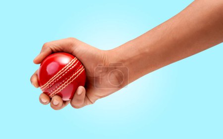 Eine männliche Hand, die ein rotes Testmatch aus Leder hält, genäht Cricketball Nahaufnahme Foto auf blauem Hintergrund