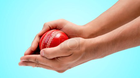 Ein Mann Hände, die den Fang eines roten Leder-Test-Cricketball Nahaufnahme Foto auf blauem Hintergrund