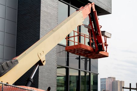 Foto de Vehículo de plataforma de trabajo aéreo durante la decoración de la fachada, elevador telescópico naranja en la obra grúa elevada - Imagen libre de derechos