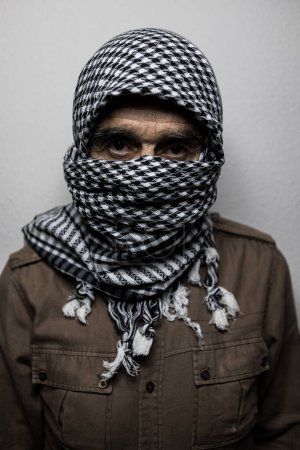 Téléchargez les photos : Portrait d'un militaire portant un foulard ou un shemagh palestinien, couvrant son visage, d'ombres dures, sur fond blanc. Concept de milicien, terrorisme, guerre, Palestine, Israël, peur, conflit. - en image libre de droit