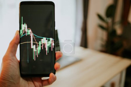 Photo for Man 30s looking stock tickers or graphs cryptocurrency trading platforms on smartphone working at home office in the morning.Close up - Royalty Free Image