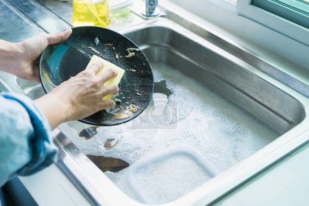 Photo for Close-up of a woman washing dishes with dirty food scraps Clean in the sink until the kitchen counter at home. - Royalty Free Image