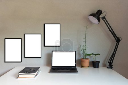 Téléchargez les photos : Moquerie d'ordinateurs portables sur fond de ciment. ordinateur personnel portable et cadre noir avec écran en papier blanc et lampe pour table, plante d'intérieur comme bureau - en image libre de droit