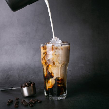 Photo for Pour milk make latte coffee into a transparent glass with ice. and roasted coffee beans in spoon on a black background studio photo - Royalty Free Image