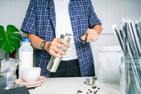 Téléchargez les photos : Barista is grinding coffee beans with manual stainless steel grinder to make black coffee machine, brewing equipment or coffee drip set Dripper on a wooden table In the kitchen at home - en image libre de droit
