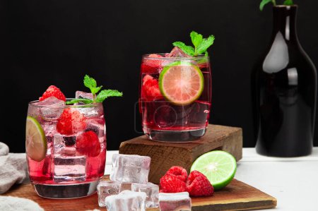 Foto de Refrescante bebida de verano con rodajas de fresa, lima y hoja de menta en vasos sobre soda de bebida de fondo oscuro - Imagen libre de derechos
