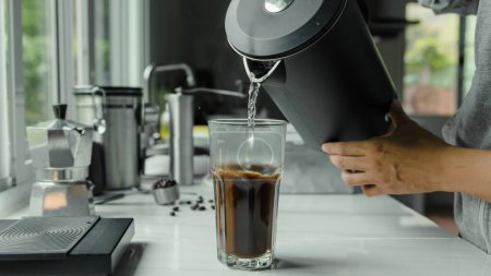 Photo for Man making use kettle pouring hot water making iced coffee or cold americano coffee into the cup with equipment, tool digital scale on the marble bar at kitchen home, Preparing drink. Close up - Royalty Free Image