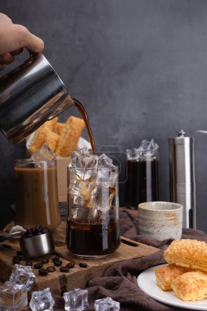 Photo for Pour milk make latte coffee, Asian iced coffee in transparent glass and roasted coffee beans and Crispy Pie on wood. black background studio photo, Copy space for your text - Royalty Free Image