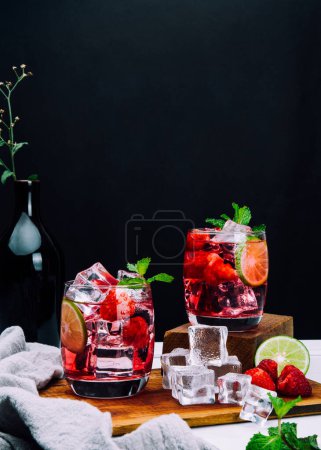 Foto de Refrescante bebida de verano con rodajas de fresa, lima y hoja de menta en vasos sobre soda de bebida de fondo oscuro - Imagen libre de derechos