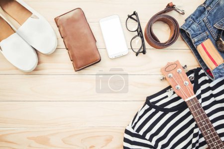 Photo for Casual apparel and accessories object clothing fashion wear with black glasses,  jeans plants, sneaks, belt white black shirt, and ukulele top view table of wooden  background copy space for tour text - Royalty Free Image