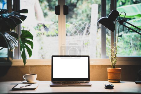 Foto de Dispositivos portátiles Mockup oficina en casa. portátil de ordenador personal pantalla blanca. y taza de café, planta de interior, anotador como un escritorio en la mañana - Imagen libre de derechos