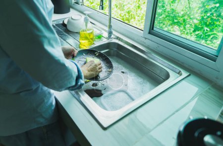 Téléchargez les photos : Gros plan d'une femme qui lave la vaisselle avec des restes de nourriture sale Nettoyant dans l'évier le comptoir de la cuisine à la maison. - en image libre de droit