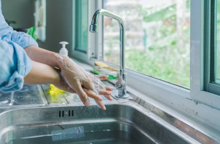 Foto de Mujer asiática con camisa azul lavándose las dos manos. limpie su dedo con agua y jabón de espuma en el fregadero de la cocina antes de comer. concepto de seguridad germinal - Imagen libre de derechos
