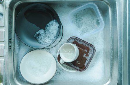 Foto de Vista superior de platos y vajilla, tazas de café en el fregadero que emplean platos con esponja y burbujas de líquido de lavado de platos, lavado y limpieza conceptos de tareas - Imagen libre de derechos