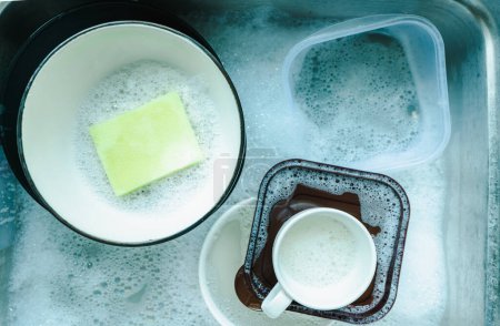 Foto de Vista superior de platos y vajilla, tazas de café en el fregadero que emplean platos con esponja y burbujas de líquido de lavado de platos, lavado y limpieza conceptos de tareas - Imagen libre de derechos