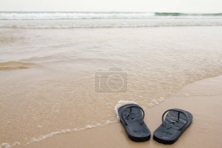 Photo for Clode up Black slippers feet on the beach, with a wave of foaming gentle beneath them. Top view - Royalty Free Image
