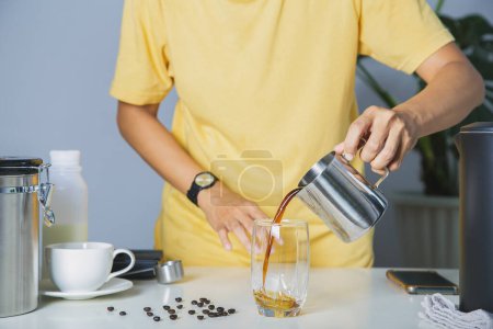 Photo for Person using pitcher Pour brewed coffee and brew cold black coffee on a mug with roasted Arabica beans on a white table and coffee maker. home made coffee - Royalty Free Image